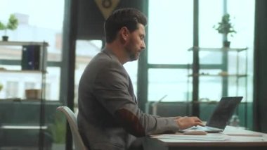 Masasında dizüstü bilgisayarı olan ve klavyesinde daktilo kullanan ciddi bir beyaz adamın görüntüsü. Bilgisayarın önünde sakallı, yakışıklı, stil sahibi bir iş adamını vurdu. Parallaks etkisi. Hız. Sinematik