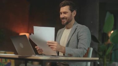 Çok mutlu iş adamının 360 derecelik izleme görüntüsü elinde belgelerle dizüstü bilgisayarda oturuyor. Şık giyinmiş heyecanlı genç adam modern ofiste el kol hareketi yaparak projeyi kutluyor. Sinema etkisi. Kamera.