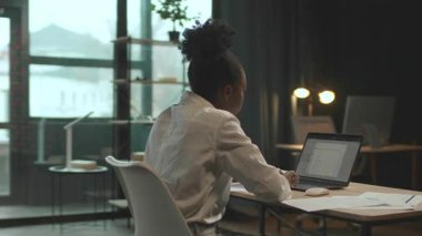 Sandalyede oturan güzel, Afro-Amerikan iş kadını ofiste çalışırken dizüstü bilgisayar kullanıyor. Ciddi görün. Kamera hareket ediyor. 360 derece