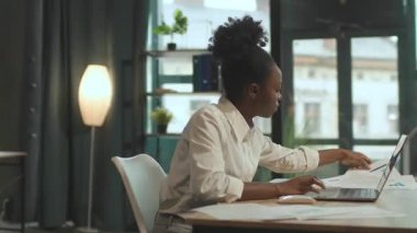 Sandalyede oturan Afro-Amerikalı iş kadınının yanında hareket eden kamera laptopta ofis kâğıdı kullanıyor. Çok ciddiyim. 360 derece