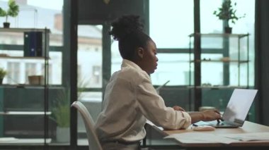 Sandalyede oturan Afrikalı Amerikalı iş kadını ofisteki klavyede dizüstü bilgisayar kullanıyor. Ciddi görün. Kamera hareket ediyor. 360 derece