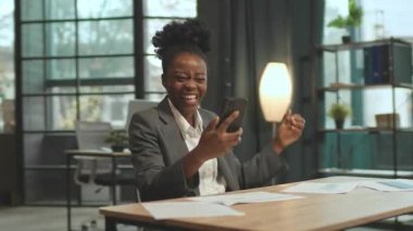 Masada oturan mutlu bayan patron akıllı telefon ekranına bakıyor. İş başarısını kutlamak için cep telefonu kullanan takım elbiseli güzel bir uzman. Çekim sırasında iz sürüyorum. İyi haber konsepti