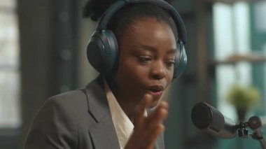 Ofiste çalışan Afrikalı Amerikalı pozitif radyo sunucusunun tam 360 izleme görüntüsü. Kulaklık takan ve konuşan genç bir kadının yakın çekim görüntüleri. Çevrimiçi konuşma. Kamera hareket ediyor