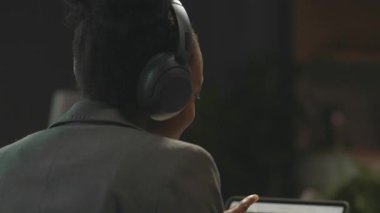 360 derecelik hızlandırılmış ofis. Genç Afro saçlı, neşeli Afrikalı Amerikalı bir kadının podcast sırasında mikrofondan konuşma görüntüsü. Mavi kulaklıklı kadın konuşmacı. Kamera hareket ediyor