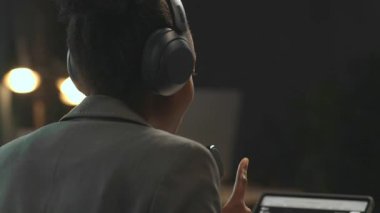 Radyodaki kayıt programı sırasında kulaklıklı gülümseyen ve mikrofonla konuşan genç bir kadının yakın çekimi. Mutlu bayan radyo sunucusu tabletteki kameraya bakıyor.