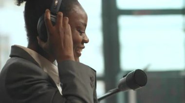 360 derece ofis çekimi. Masada otururken dans eden neşeli Afro-Amerikan kadın. Kadın radyo sunucusu podcast yaparken eğleniyor, kendini ifade ediyor. Çekim etrafında hareket eden izleme