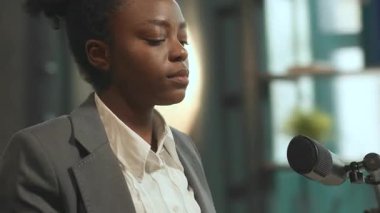 İyi görünümlü Afro-Amerikan bayan radyo sunucusu mikrofonun önünde oturmuş, kulaklık takıyor. Müzik dinleyen takım elbiseli genç bir kadın. Müzikal duraksama konsepti. Kamera hareket ediyor