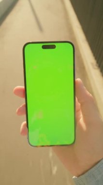 Açık havada yeşil ekranlı akıllı telefon kullanan genç adamın yakın çekim görüntüleri. Eski binayla caddenin bulanık arka planında cep telefonu kullanan bir erkek. Dijital konsept
