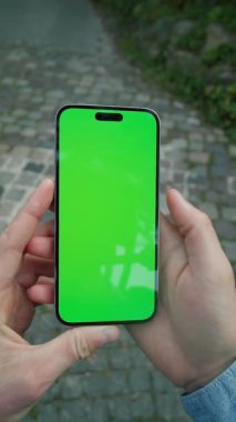 Akıllı telefondan erkek eli çekmek. Beyaz bir gencin sosyal medyada gezinen görüntüsü caddenin bulanık arka planında, dışarıda kaldırım taşları var. Dijital iletişim konsepti