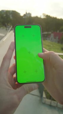 Yeşil ekranlı, el ele tutuşan adamların yakın çekimi. Genç adam telefon ve maket kullanıyor. Arka planda, açık havada antik mimari. Yatay görüntü. Dışarıda.