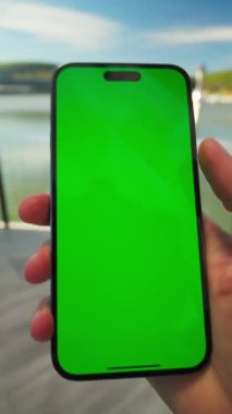 Yeşil ekranlı akıllı telefonun yakın görüntüsü. Cep telefonu erkek elinde. Kromakey ekranlı akıllı telefon görüntüsü. Tanınmayan bir adam gölün güzel manzarasını çekmek için yaklaşıyor.