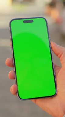 Sokakta izole edilmiş yeşil ekranlı siyah akıllı telefonlu kot pantolonlu beyaz erkek eli yakın plan fotoğrafı. Gündüz vakti. Güneşli bir gün. Açık hava.