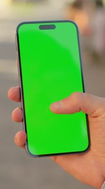 Mavi gömlekli, elinde yeşil ekranlı, arka planda bulanık sokak olan siyah akıllı telefonlu adamların görüntüsü. Krom tuş ekranında kaydıran ve dokunan adam