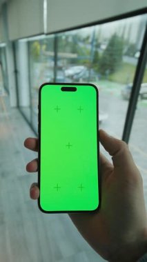 Kapalı alan görüntüsü, yeşil ekranlı, el kamerasının tutuşu ve dikey olarak telefonu kaydırması. Arka planda büyük pencereli modern alan. Akıllı telefondan yazıyorum.
