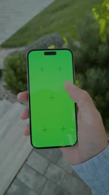 Adamın elleri yeşil ekranlı dikey telefonu tutuyor ve kaydırıyor. Arka plandaki merdivenlerde. Doğa otu