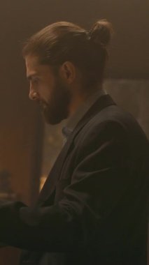 Sakallı genç iş adamı, masa başında oturup kağıtlarla çalışmayı düşünür. Gece ofisindeki bilgisayarı kullan. İşine odaklan. Akşam ışığı