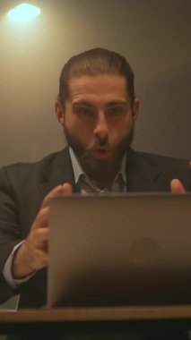 Yakın çekim çekici sakallı iş adamı masasına oturup gülümsüyor ve işte dans ediyor. Gece ofisinde dizüstü bilgisayar kullan