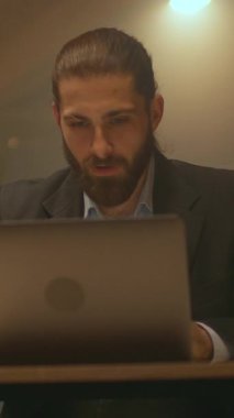 Çekici sakallı iş adamı masasında oturup çalışırken mutlu bir şekilde gülümsüyor. Gece ofisinde dizüstü bilgisayar kullan