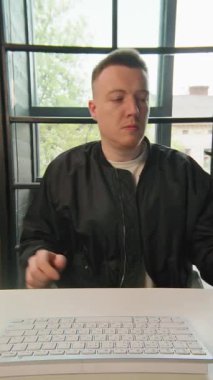 Ofiste kulaklık takan genç adam bilgisayarla çalışıyor kameraya gülümsüyor bak. Pozitif iş adamının portresi