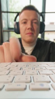 Ofiste bilgisayarda çalışan ve daktilo yazan kulaklıklı gülümseyen genç adam. Ön plandaki klavyede. Pozitif iş adamının portresi