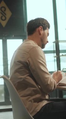 Masada oturan iş adamı not defterine not alır klavyeye dizüstü bilgisayar kullanır. Düşünüyorum. Kamera hareket ediyor. 360 Derece