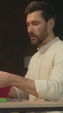 Masada oturan mutlu sakallı bir adam sosyal medyada yazarken gülümsüyor ve şarkı söylüyor. Modern ofis. Kamera hareket ediyor. 360 Derece