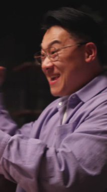 Gözlüklü yakışıklı Asyalı genç adam gece evde sosyal medyada cep telefonuyla sohbet ediyor. 360 derece. Kamera hareket ediyor