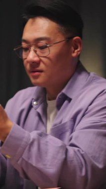 Evde gözlüklü Asyalı bir adam gece sosyal medyada cep telefonuyla sohbet ediyor. 360 derece. Kamera hareket ediyor