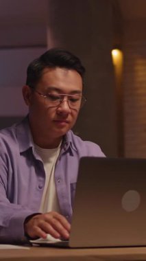 Merak ediyorum, gözlüklü Asyalı adam cep telefonu kullanıyor sosyal medyada sohbet ediyor gece evde mutlu dans ediyor. 360 derece. Kamera hareket ediyor