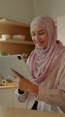 Mutfakta Müslüman bir kadın evdeki sandalyede oturan tablet bilgisayar kullanıyor. Kamera hareket ediyor. 360 derece