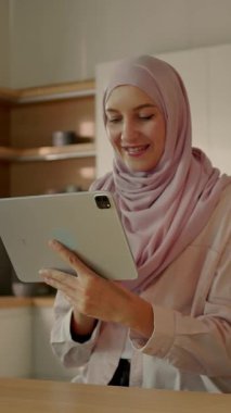 Mutlu Müslüman kadın güneş ışığı mutfağındaki masa başında tablet bilgisayar kullanıyor. Evde. Kamera hareket ediyor. 360 derece