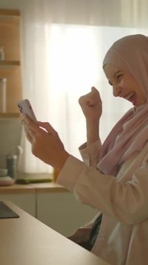 Kameralar tesettürlü müslüman kadının yanında hareket ediyor telefon kullanıyor ve ev mutfağında gün ışığında gülümsüyor. 360 derece