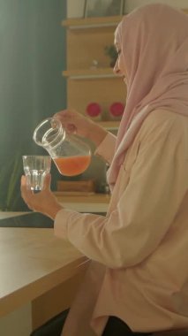 Modern aydınlık mutfakta masada oturmuş domates kesen tesettürlü güzel müslüman kadın. Sebze. Kamera hareket ediyor. 360 derece