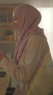 Modern mutfakta tesettürlü mutlu müslüman kadın gün ışığında gülümseyen telefonu kullanır. Kamera hareket ediyor. 360 derece