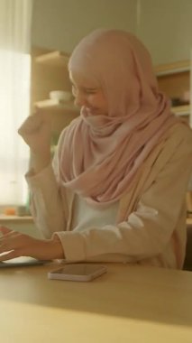 Sırıtan müslüman iş kadını dizüstü bilgisayar başında çalışırken evde mutlu oluyor. Güneş ışığı. Kamera hareket ediyor. 360 derece