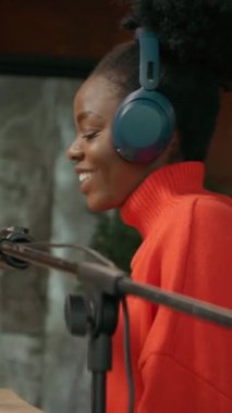 İş yerinde oturan, kulaklıklı, gülümseyen, Afro-Amerikan güzel bir kadının yatay görüntüleri. Çalışırken mikrofon kullanan kadın radyo sunucusu. Dijital tablet kullanan bir kız. Parallaks