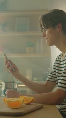 Sarı akıllı telefonu elinde tutan neşeli, genç, beyaz bir adam ekrandaki alete bakıyor. Mutfakta mesaj okuyan mutlu adam. İz sürme hareket ediyor. İçeride. Parallaks etkisi