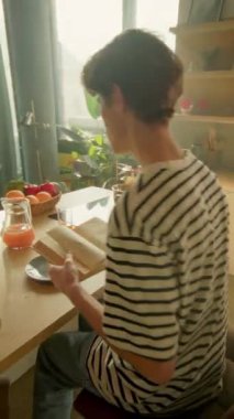 Yakışıklı beyaz bir adam bardağa portakal suyu döküyor. Mutfaktaki kahvaltı masasında oturan adamın görüntüsü. Sağlıklı yaşam tarzı kavramı. İçeride. Dönme açısı. Parallaks etkisi. Günaydın.