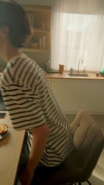 Kafkasyalı genç adam elinde kitap tutuyor ve kahvaltı masasında otururken portakal suyu içiyor. Modern rahat stüdyoda kitabı rafa koyan adam. 360 derecelik izleme atışı