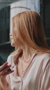 Modern otel odasının lüks içinde, kızıl saçlı, akıllı telefondan mesaj atan zarif, güzel bir kadın. Kendine güveni tam başarılı bir iş kadını, aletin üzerinde sohbet ediyor.