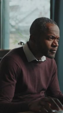 Bilgisayarlı ve evde çalışan dalgın bir Afrikalı adam. Gülümseyen serbest çalışan, ekranlara bakıp içeride makale yazmaya odaklanmış. Gündüz