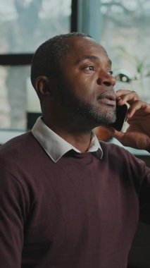 Ciddi bir iş adamının yatay olarak vurulması sohbete ve jestlere odaklandı. Rahat, modern oturma odasında akıllı telefondan konuşan Afro-Amerikalı bir adam. Kapalı