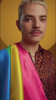 Lgbt bayrağını omuzunda taşıyan adamın dikey çekimi sarı arkaplandaki kameraya bakıyor