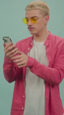 LGBT güneş gözlüklü genç adam stüdyoda telefonla gülümsüyor. Dikey çekim