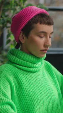 Açık yeşil kazaklı, ikili olmayan birinin iş yerinde kameraya baktığı bir fotoğraf.