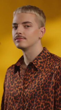 Çekici eşcinsel adam kameraya bakar sarı arka plandaki yeşil yapraklara gülümser.