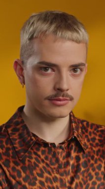 Stüdyoda leopar desenli tişörtlü genç bir adamın sarı arka plandaki kameraya bakarken ki görüntüsü.