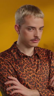 Leopar gömlekli genç sarışın adam elleri göğsünde kameraya bakıyor.