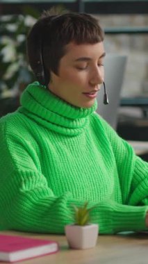 Diz üstü bilgisayarda oturan ve çağrı merkezinde mikrofon başında konuşan transseksüel kişi.