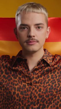 İçerde gökkuşağı bayrağı tutarken kameraya gülümseyen genç eşcinsel adam.